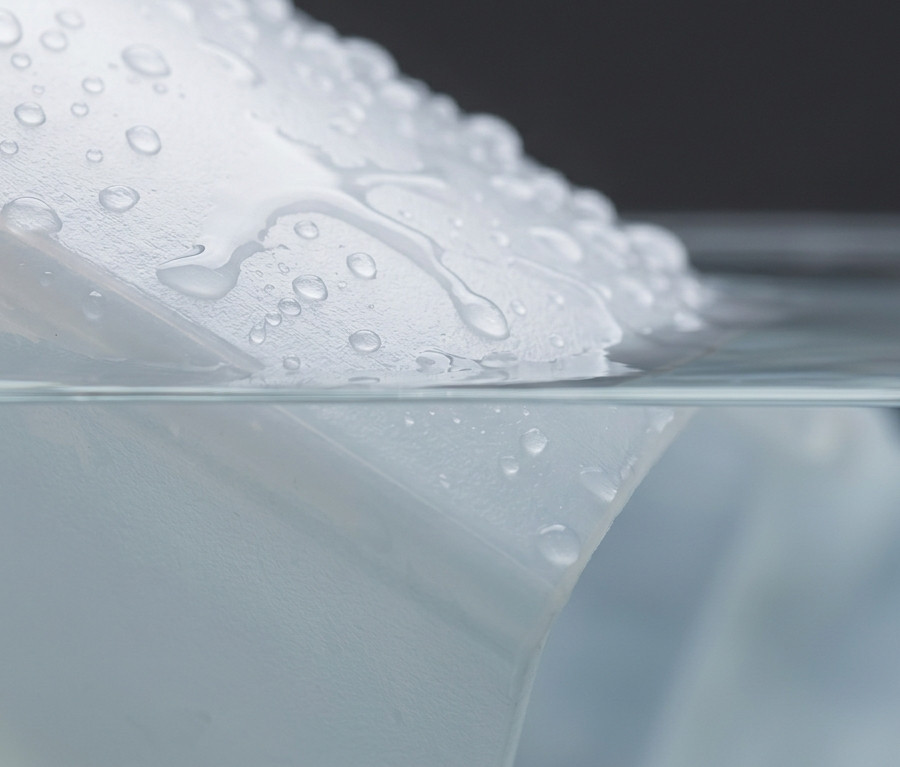 Close-up of a natural polyethylene surface at the waterline, showing water beading on the exposed face with no visible reaction at the submerged interface.
